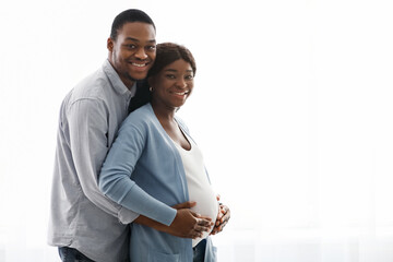 Smiling black man hugging his pregnant woman over white background