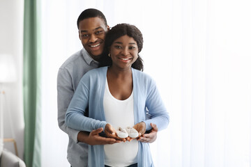 Wall Mural - Happy pregnant african american family holding small baby shoes