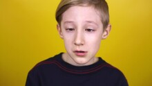 The Boy Brings His Eyes Together And Then Laughs. The Child Stands Against A Yellow Background And Shows Emotions