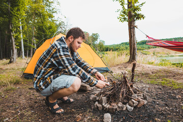 Wall Mural - young strong man light a fire at camping site yellow tent on background