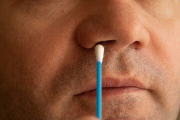 The man brings a cotton swab to his nose. Cleaning the nose