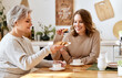 © JenkoAtaman - Cheerful mother and daughter drinking coffee at home