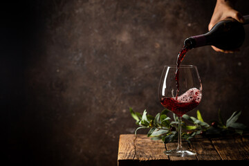 Pouring red wine into the glass against rustic dark wooden background