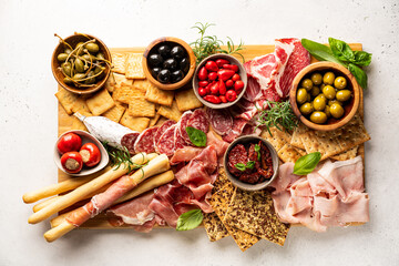 Appetizers with differents antipasti, charcuterie, snacks and red wine on white background. Sausage, ham, tapas, olives and crackers for buffet party. Top view, flat lay