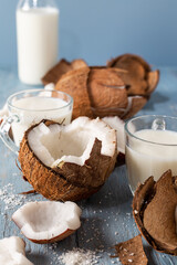 Wall Mural - Coconut halves and pieces with glass of coconut milk on a blue natural wooden background.