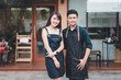 © amnaj - Young Asian couple in apron standing in front of his shop.