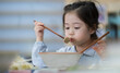 Asian child eat noodle in the cup by the chopsticks. Little asian child girl having breakfast at the morning with a happy smiling face