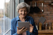 © fizkes - Learn using gadgets. Active smiling middle aged latin female pensioner use modern tablet computer at kitchen. Happy mature grandmother hold digital pad search information online read electronic book