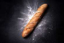 Crispy French Baguette In Splashes Of Wheat Flour On A Black Background.