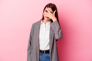 Wall Mural - Young caucasian business woman isolated on pink background blink at the camera through fingers, embarrassed covering face.