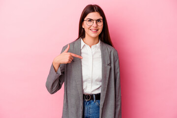 Young caucasian business woman isolated on pink background person pointing by hand to a shirt copy space, proud and confident