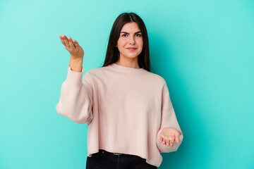 Young caucasian woman isolated on blue background makes scale with arms, feels happy and confident.