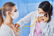Doctor in mask checking up on female patient using stethoscope