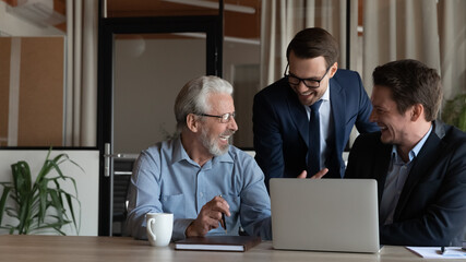 Poster - Overjoyed diverse male colleagues brainstorm cooperate on computer in modern office together. Multiethnic businessmen or business partners talk laugh discussing collaboration. Teamwork concept.