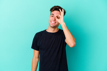 Young caucasian man isolated on blue background excited keeping ok gesture on eye.