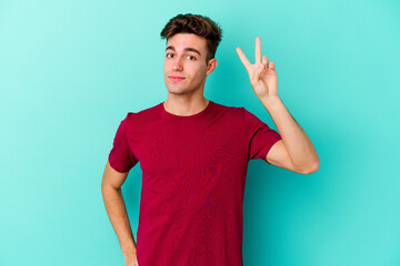 Wall Mural - Young caucasian man isolated on blue background joyful and carefree showing a peace symbol with fingers.