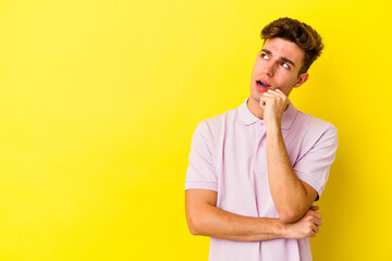 Young caucasian man isolated on yellow background relaxed thinking about something looking at a copy space.