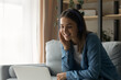 © fizkes - Close up smiling woman wearing headphones chatting, using laptop, looking at computer screen, sitting on couch at home, happy young female making video call to relatives or friends, talking