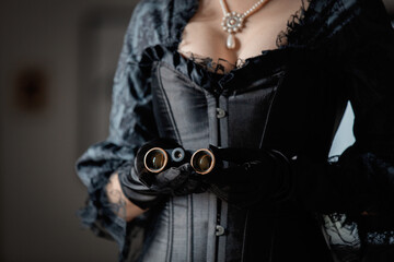 Beautiful woman in vintage black dress holding an opera glasses in indoor