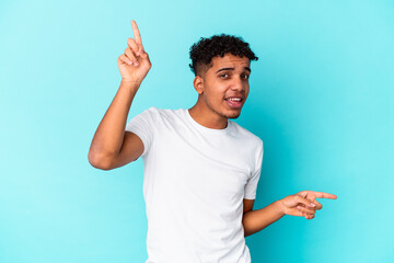 Young african american curly man isolated on blue pointing to different copy spaces, choosing one of them, showing with finger.