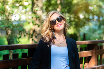 Wall Mural - fashion portrait of a stylish nice blonde female in sunglasses on a defocused park background