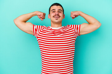 Young caucasian man isolated on blue background showing strength gesture with arms, symbol of feminine power