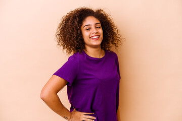 Wall Mural - Young african american woman isolated on beige background confident keeping hands on hips.