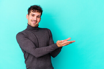 Wall Mural - Young caucasian man isolated on blue background holding a copy space on a palm.