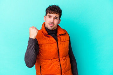 Wall Mural - Young caucasian man isolated on blue background showing fist to camera, aggressive facial expression.