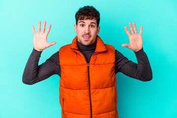 Wall Mural - Young caucasian man isolated on blue background showing number ten with hands.