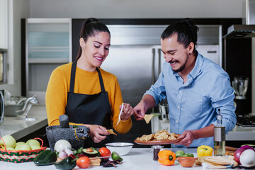 Poster - mexican couple cooking and eating mexican food sauce together in their kitchen at home in Mexico city