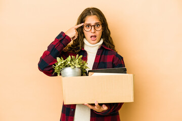 Wall Mural - Young caucasian woman moving holding a box isolated showing a disappointment gesture with forefinger.