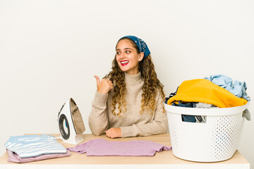 Wall Mural - Young caucasian woman ironing clothes isolated points with thumb finger away, laughing and carefree.