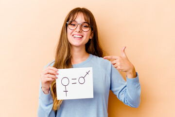 Wall Mural - Young caucasian woman holding a equality gender placard isolated person pointing by hand to a shirt copy space, proud and confident