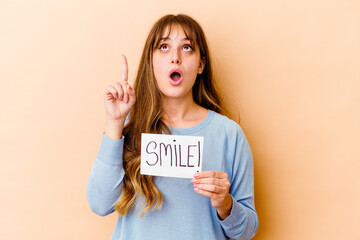 Wall Mural - Young caucasian woman holding a Smile placard isolated pointing upside with opened mouth.