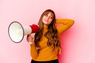 Wall Mural - Young caucasian woman holding a megaphone isolated touching back of head, thinking and making a choice.