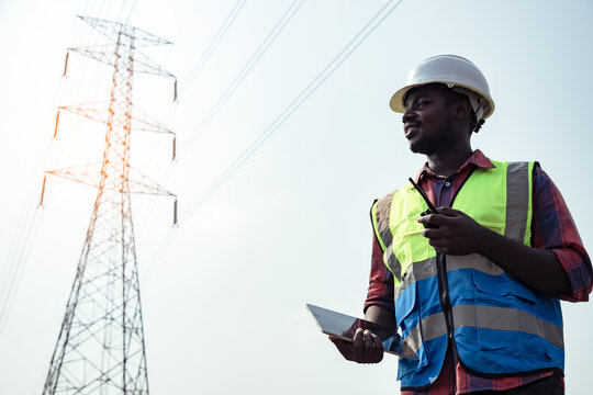 electrical africa american engineer with high voltage electricity pylon and using walkie talkie and 