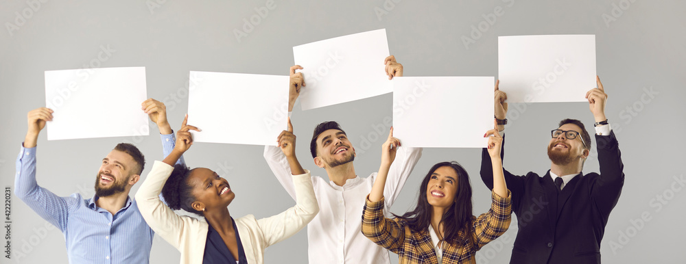 Banner with group of five happy smiling diverse people, colleagues or friends, expressing opinion and giving positive feedback holding white mockup signs and sheets of paper on gray studio background - obrazy, fototapety, plakaty 