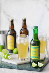 Bottle and glass of fresh ginger beer on light background