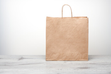 Paper bag with handles isolated. Kraft paper bag mockup on wooden table. Recycled shopping bag for product or food home delivery.