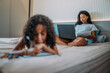 © Nexa - latinx curly haired girl doing homework in bed with mother.