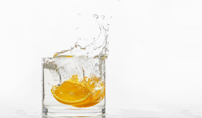 glass container with liquid, fallen orange slices, splash of water on a white background