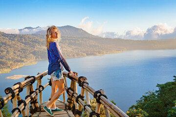 Wall Mural - Summer family vacation. Young woman stand at balcony on high cliff. Happy girl looking at amazing tropical jungle view. Buyan lake is popular travel destinations in Bali island, Indonesia