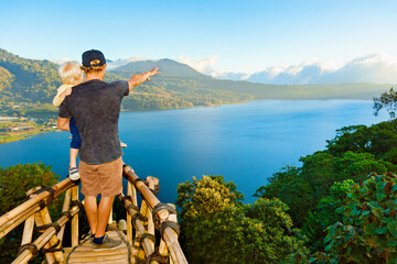 Wall Mural - Summer family vacation. Young father with baby son stand at balcony on high cliff. Happy child look at amazing tropical jungle view. Buyan lake is popular travel destinations in Bali island, Indonesia