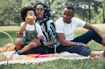 Happy picnic relax black people family with son blowing bubbles in garden