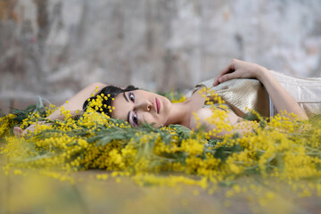 Dark-haired sensual woman on the floor among mimosa flowers