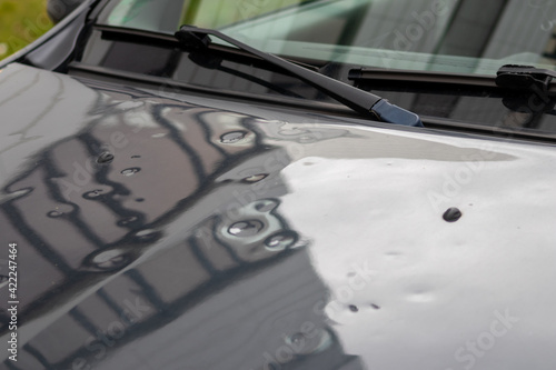 Car engine hood with many hail damage dents show the forces of nature and the importance of car insurance and a replacement value insurance against hail storm and storm hazards or extreme weather