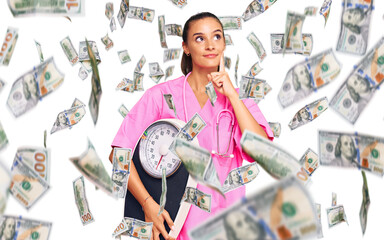 Wall Mural - Young hispanic woman as nutritionist doctor holding weighing machine serious face thinking about question with hand on chin, thoughtful about confusing idea