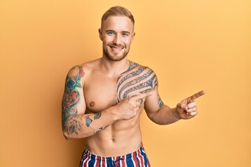 Wall Mural - Young caucasian man wearing swimwear shirtless smiling and looking at the camera pointing with two hands and fingers to the side.