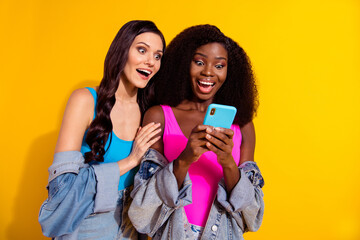 Wall Mural - Photo of impressed nice brunette hairdo ladies look telephones wear bright tops jeans shirts isolated on yellow color background